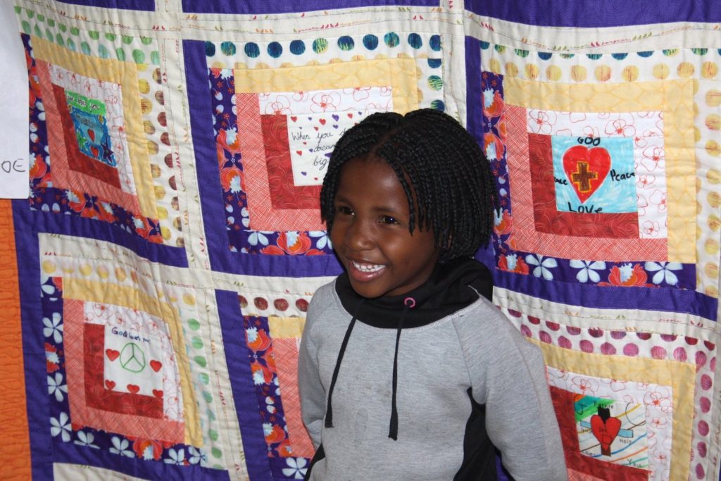 A child standing in front of a quilt hung on a wall