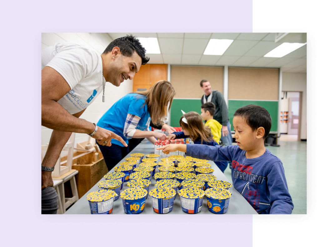 here is a man giving a hungry child a lunch in a school classroom